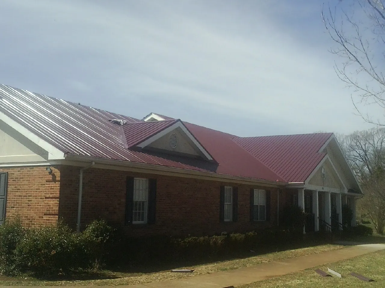 Red metal roof with gabled entries on a long brick building, from a Hail Damage Roof Repair job in Rescue