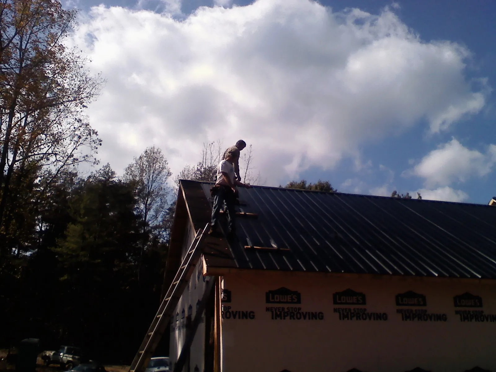 Roofer fastening dark metal panels high against a cloudy sky, from a Roof Inspection job in Rescue
