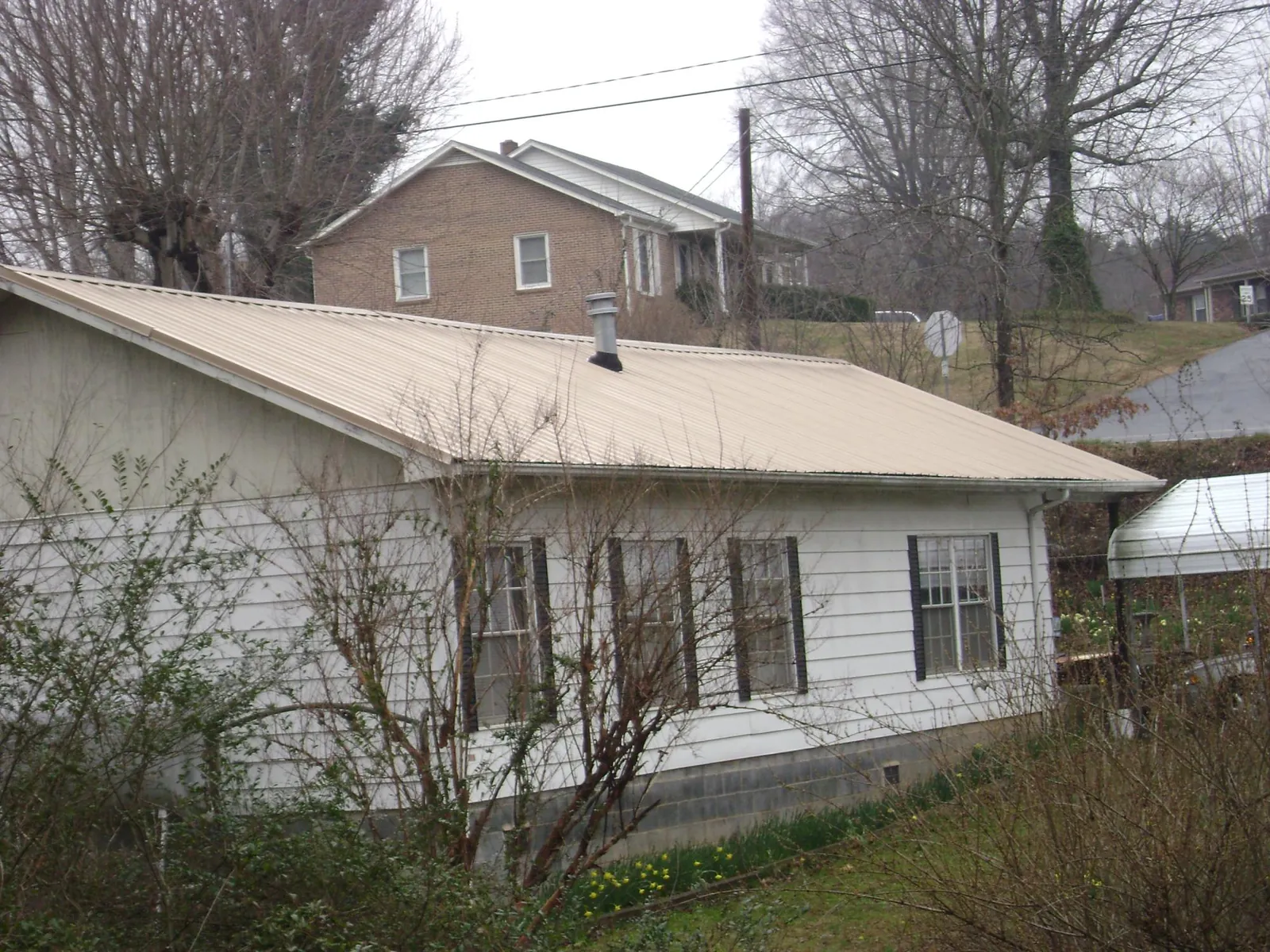 Tan metal roof on a white sided house set into a hillside in Rescue